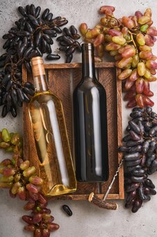 Duas garrafas de vinho com uvas e taças de vinho no antigo fundo de mesa de concreto cinza com espaço de cópia. vinho tinto com um ramo de videira. composição de vinho em fundo rústico. brincar.