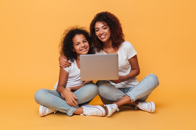 Duas irmãs afro-americanas sorridentes segurando computador portátil