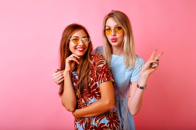 Duas irmãs bonitas felizes, melhores amigas, mulheres hipster se divertindo juntas no fundo rosa do estúdio