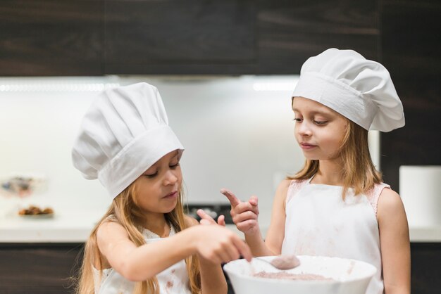 Duas irmãs, em, cozinha, desgastar, chapéu cozinheiro, olhar, messy, dedo, enquanto, levando cacau, pó