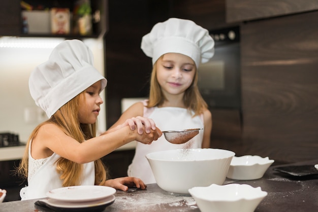 Duas irmãs fofos peneirando o cacau em pó através de filtro na cozinha