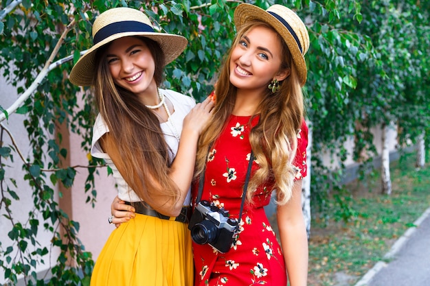 Duas irmãs muito jovens felizes, abraços, sorrindo, rindo e se divertindo malucos juntos, carregando roupas femininas vintage retrô elegantes e chapéus. ao ar livre.