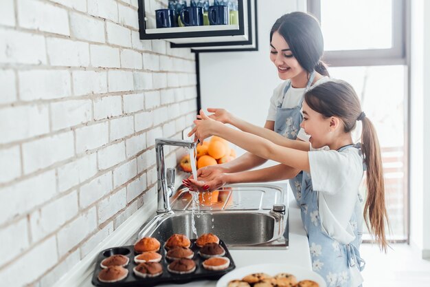 Duas irmãs sorridentes lavando as mãos na cozinha de casa