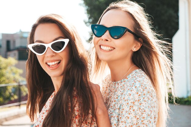 Duas jovem e bela mulher hipster sorridente em vestidos de verão da moda Mulheres despreocupadas sexy posando na rua Modelos puros positivos se divertindo no pôr do sol abraçando e enlouquecendo Feliz e alegre