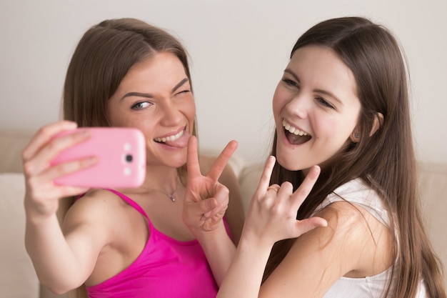 Duas jovens amigas felizes tomando selfie com smartphone.