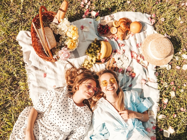 Duas jovens belas sorrindo hipster feminina em um vestido de verão na moda e chapéus. Mulheres despreocupadas fazendo piquenique do lado de fora.