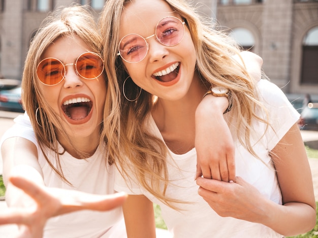 Duas jovens bonitas loiras garotas hipster sorridente em roupas de camiseta branca na moda verão.