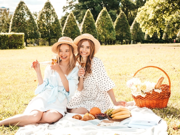 Foto grátis duas jovens bonitas sorrindo hipster fêmea com vestido de verão e chapéus. mulheres despreocupadas fazendo piquenique do lado de fora.