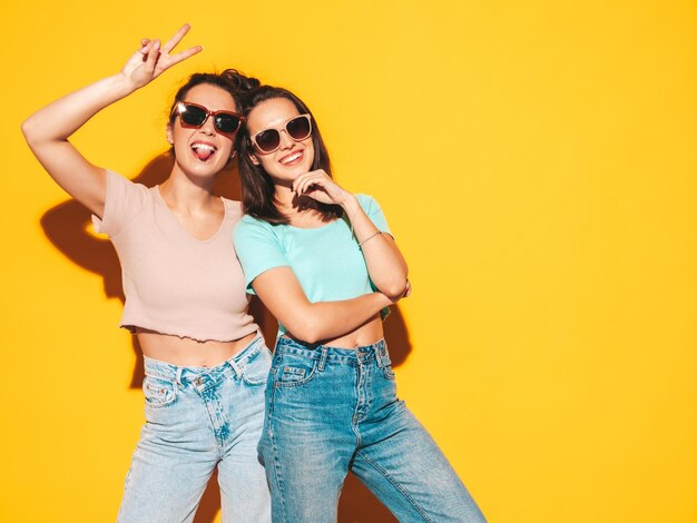 Duas jovens lindas e sorridentes hipster loira em roupas da moda de verão Mulheres despreocupadas sensuais posando no estúdio Modelos positivos se divertindo Alegre e feliz