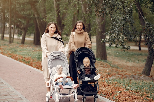 Duas jovens mães andando em um parque de outono com carruagens