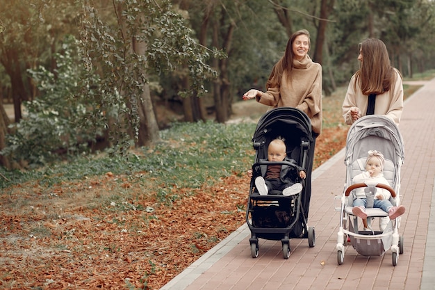 Duas jovens mães andando em um parque de outono com carruagens
