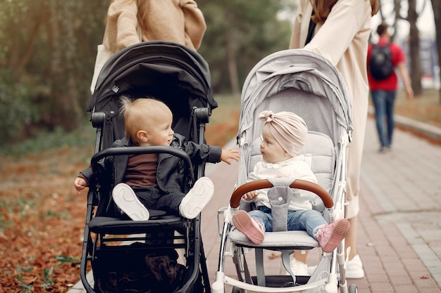 Duas jovens mães andando em um parque de outono com carruagens