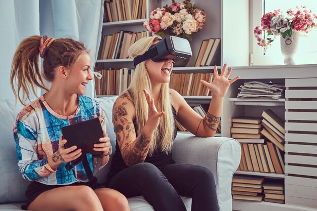 Duas jovens namoradas em roupas casuais se divertindo com dispositivo de óculos de realidade virtual em casa.