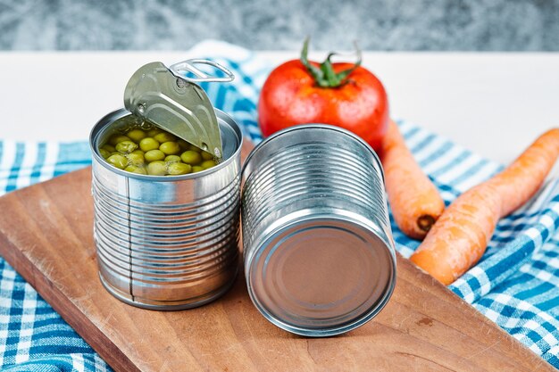 Duas latas de ervilhas cozidas, legumes e toalha de mesa sobre uma mesa de mármore e branco.