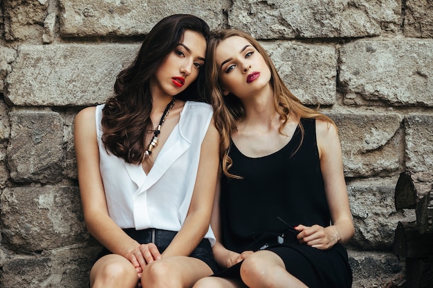 Duas lindas meninas sentadas em frente a um velho muro de pedra