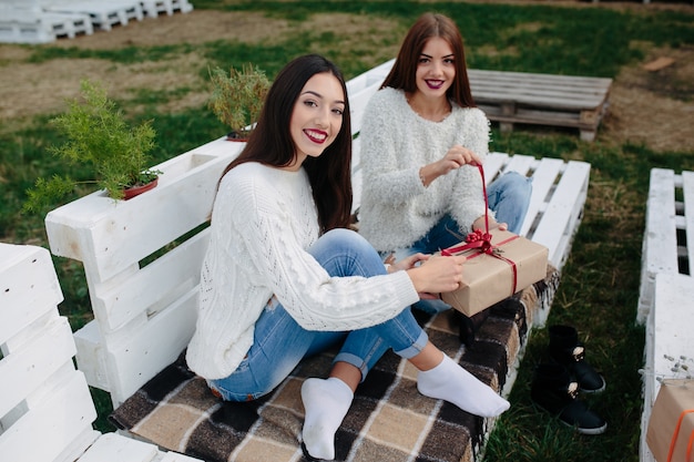 Duas lindas mulheres sentadas em um banco segurando presentes nas mãos