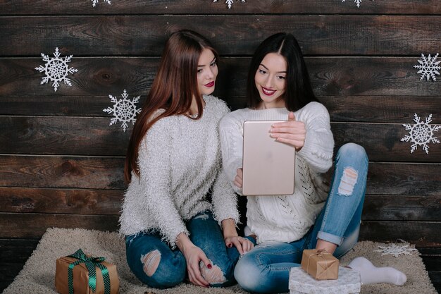 Duas lindas mulheres sentadas no chão com um tablet, entre os presentes de Natal