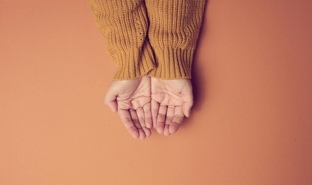 Duas mãos femininas dobradas palma a palma em um fundo laranja, vista superior