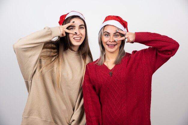 Duas meninas com chapéu de Papai Noel em pé e posando.