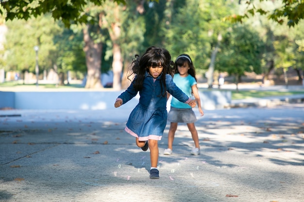 Duas meninas de cabelos negros animadas jogando amarelinha no parque da cidade. comprimento total, copie o espaço. conceito de infância