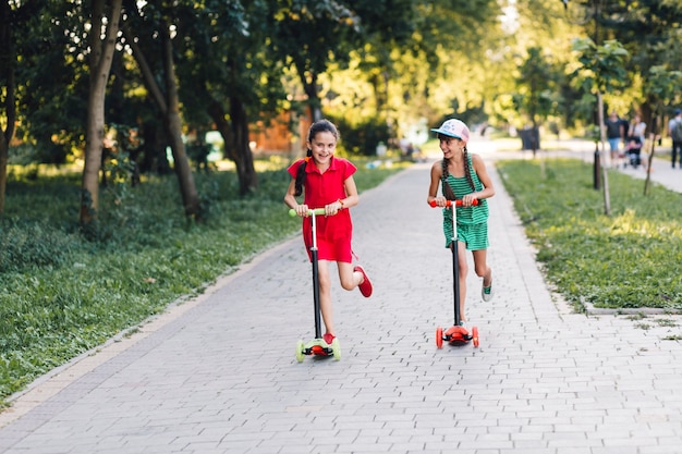Duas meninas, desfrutando, montando empurrar scooter, parque
