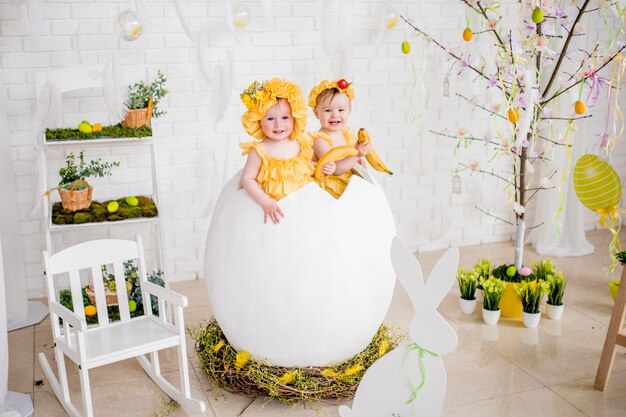 Duas meninas em vestidos amarelos sentar em um ovo no estúdio