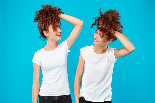 Duas meninas gêmeas segurando o cabelo, brincando sobre parede azul