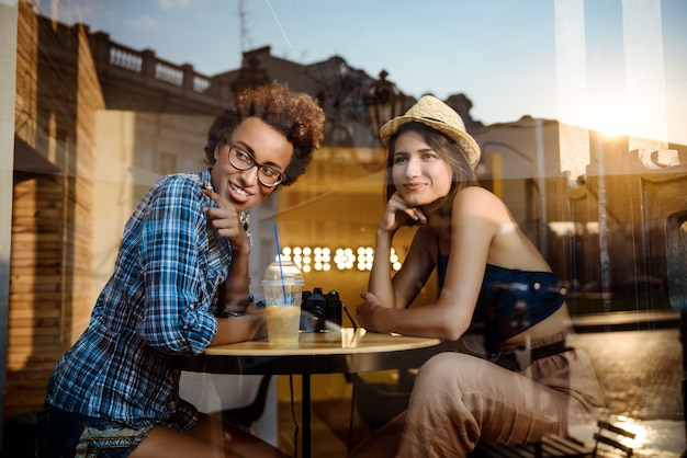 Duas meninas lindas sorrindo, falando, descansando no café. Atirado de fora.