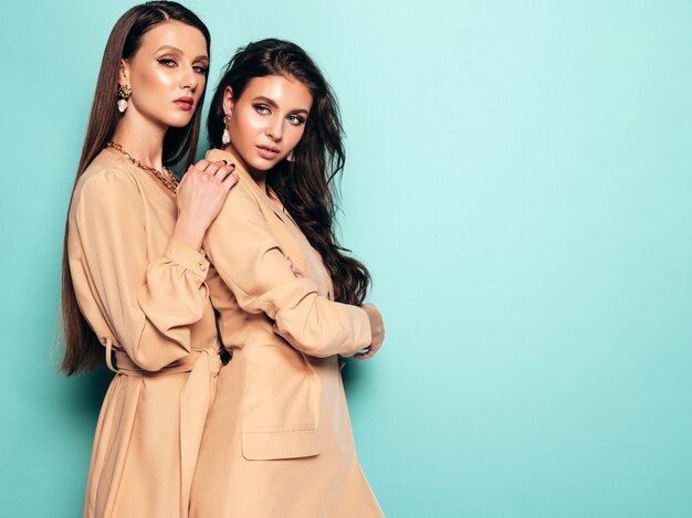 Duas meninas morenas lindas em roupas de verão na moda agradável. Mulheres despreocupadas sexy posando perto da parede azul no estúdio