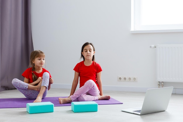 Duas meninas praticando ioga, alongamento, fitness por vídeo no notebook. treinamento de educação online à distância, aeróbio em casa. estilo de vida saudável, coronavírus, fique em casa. crianças usam quarentena em casa.