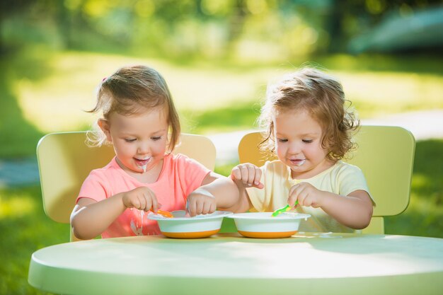 Duas meninas sentadas em uma mesa e comer juntos contra o gramado verde