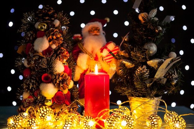 Duas mini árvores de natal e uma estatueta de papai noel em fundo preto com luzes de bokeh nele