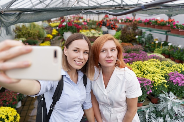 Duas moças lindas fazendo selfie em fundo de flores na estufa