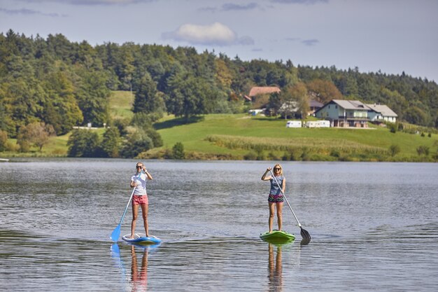 Duas mulheres andando de prancha de stand up paddle no lago Smartinsko, na Eslovênia