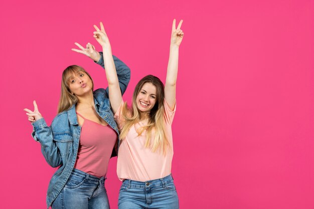 Duas mulheres com as mãos levantadas em fundo rosa