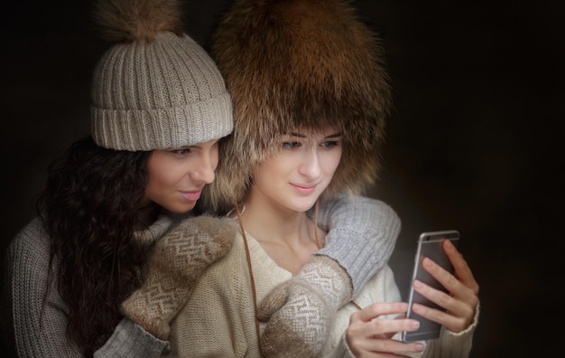 Duas mulheres com chapéus de inverno e camisolas tomando selfie com smartphone.