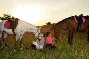 Foto grátis duas mulheres e dois cavalos ao ar livre no verão feliz pôr do sol junto a natureza