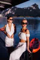 Foto grátis duas mulheres elegantes com roupas brancas de verão e óculos escuros perto do mar