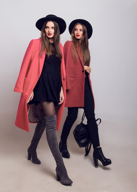 Duas mulheres elegantes com um casaco casual moderno de primavera, botas com salto, chapéu preto e bolsa estilosa