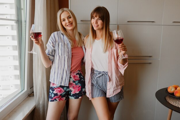 Duas mulheres felizes e despreocupadas, olhando para a janela e segurando um copo de vinho. atmosfera caseira acolhedora.