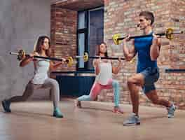 Foto grátis duas mulheres fitness e um treinador, esticando agachamentos com halteres em um clube com interior loft.