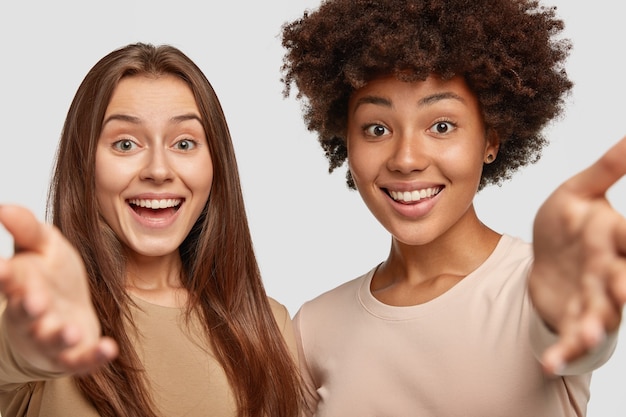 Foto grátis duas mulheres jovens de raça mista têm expressões amigáveis positivas e mantêm-se próximas uma da outra