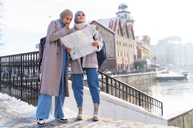 Duas mulheres muçulmanas com hijabs consultando um mapa enquanto viajam na cidade