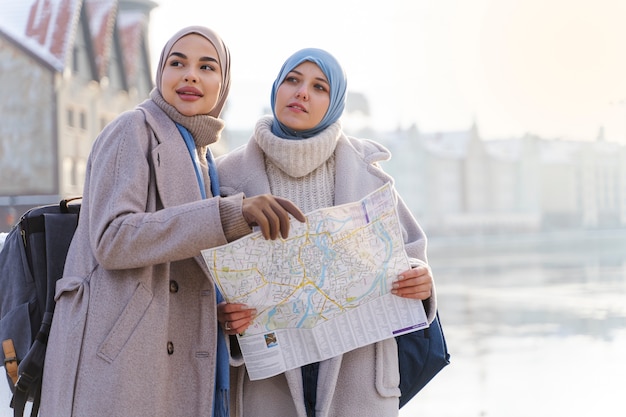 Duas mulheres muçulmanas com hijabs consultando um mapa enquanto viajam na cidade