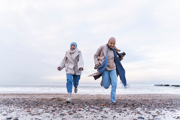 Duas mulheres muçulmanas com hijabs correndo na praia durante a viagem