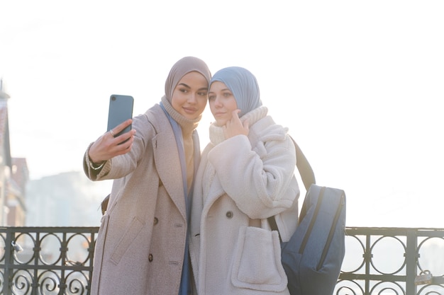 Duas mulheres muçulmanas com hijabs tirando uma selfie enquanto viajam na cidade
