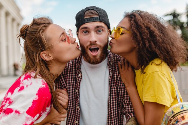 Duas mulheres se beijando em uma emoção feliz e animada, uma jovem companhia de amigos sorridentes se divertindo juntos