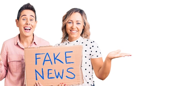 Foto grátis duas mulheres segurando um banner de notícias falsas comemorando a vitória com sorriso feliz e expressão vencedora com as mãos levantadas