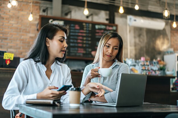 Duas mulheres sentadas e trabalhando com um laptop em uma cafeteria