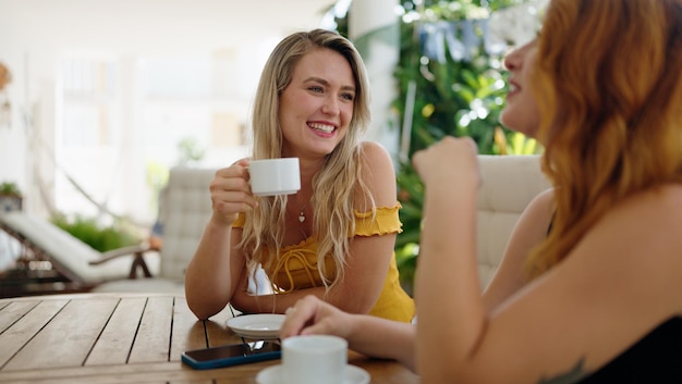 Duas mulheres sentadas na mesa conversando e tomando café no terraço de casa